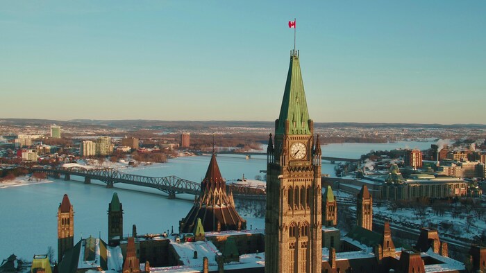علم كندا يرفرف على قبة برج السلام وهو جزء من مبنى البرلمان الكندي في أوتاوا، وتبدو في الصورة مبانٍ أخرى تابعة للبرلمان إضافة إلى اثنين من الجسور فوق نهر أوتاوا.