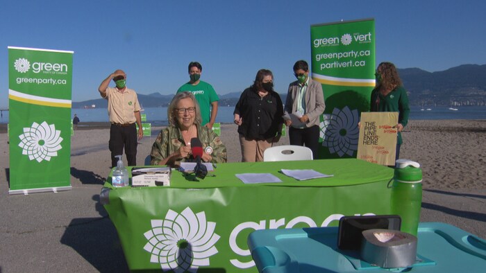 Des candidats du Parti vert du Canada se préparent à s'adresser aux médias, entourés de bannières, sur la plage.