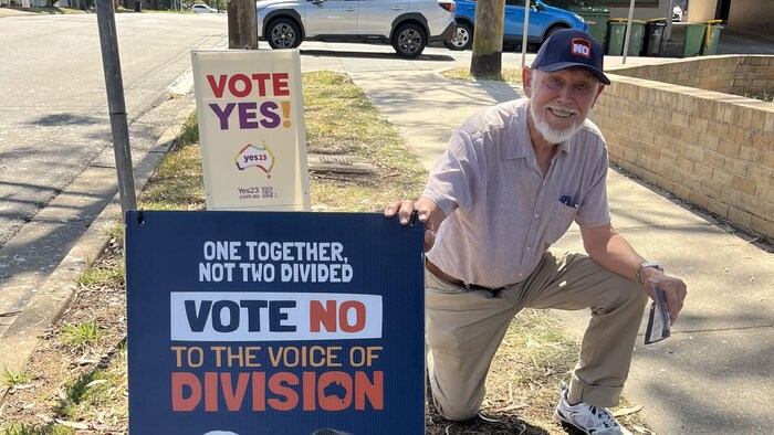 Ray Devney crouches next to an election symbol.