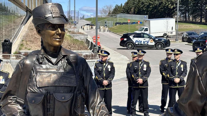 Des policiers en tenue de cérémonie se tiennent derrière une sculpture en bronze d'officiers se tendant la main.
