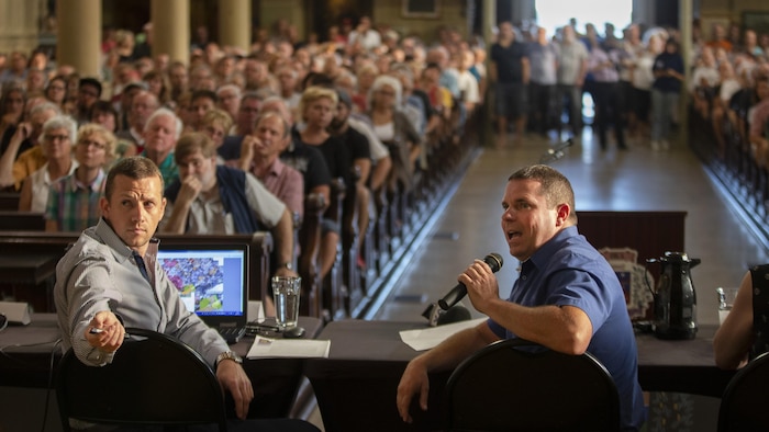 M. Quevillon, au premier plan, devant des bancs remplis, plusieurs personnes étant aussi debout à l'arrière.