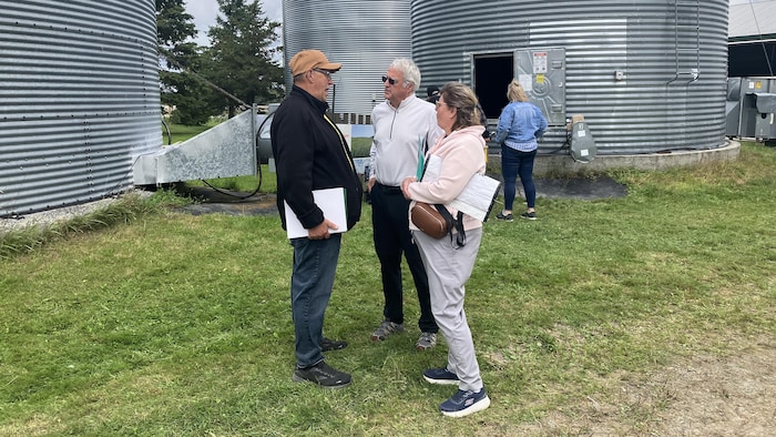 Pascal Rheault et Pierre Dufour échangent sous les yeux d'une dame sur le site d'une ferme.