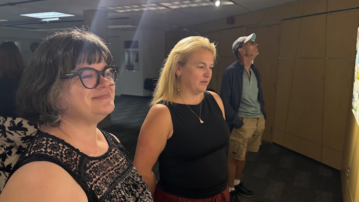 Trois personnes admirent des tableaux sur un mur.