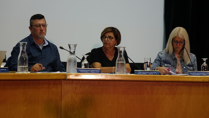 Un conseiller et deux conseillères municipaux assis à la table d'un conseil de ville.