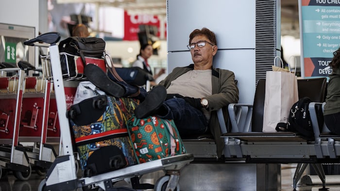 Un passager en attente à l'aéroport Pearson de Toronto, assis avec les pieds sur ses valises, le 15 août 2025.