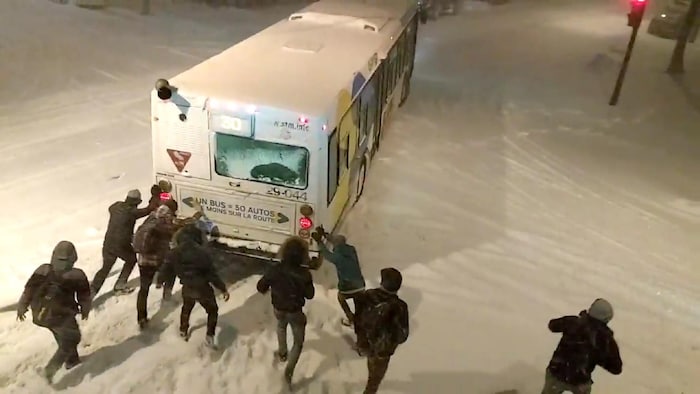 بعض المارة يساعدون حافلة نقل مشترك في مونتريال على التحرر من الثلوج التي تعيق انطلاقتها.