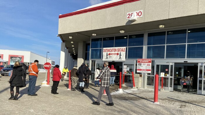 Des clients font la file à l'extérieur d'un commerce l'hiver.