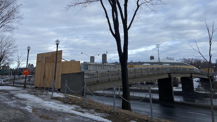 Une passerelle piétonnière est bloquée par des panneaux de bois près d'une affiche orange Trottoir barré.