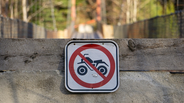 Une affiche sur laquelle on voit un VTT avec un cercle rouge et une barre transversale qui indique que ce genre de véhicule ne peut pas passer.