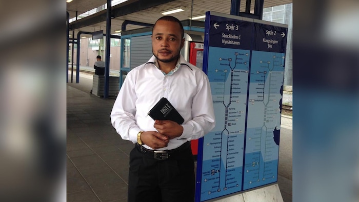 Un homme debout sur le quai d'une gare de train tient un exemplaire de la Bible entre ses mains.