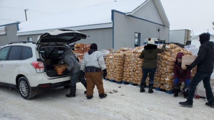Des centaines de sacs de patates dans la neige. Des gens se promènent avec des boîtes.