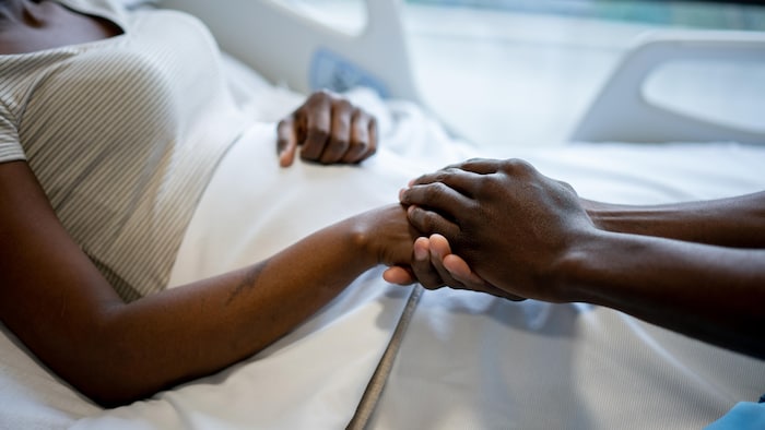 Une patiente dans un lit d'hôpital se fait tenir la main par une personne.