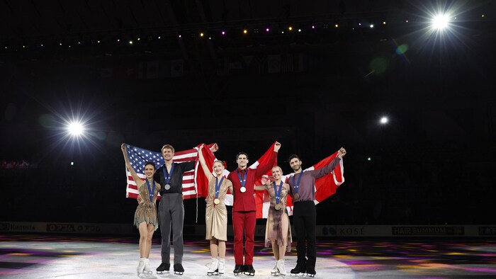 Les deux duos canadiens et le duo américain posent sur la glace avec leurs médailles et leurs drapeaux respectifs.