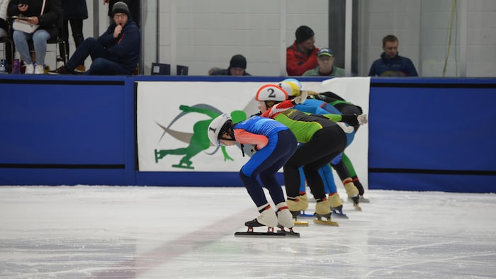 Cinq patineurs sur la glace sont en position de départ.