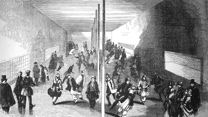Des patineurs des deux sexes chaudement vêtus s'activent sur une patinoire intérieure soutenue par une rangée de piliers, au centre, et bordée par de larges fenêtres qui laissent entrer l'air froid. 