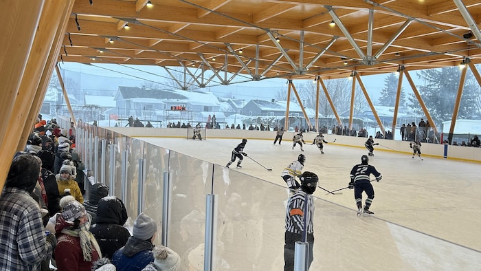 Une partie de hockey sur une patinoire extérieure couverte.