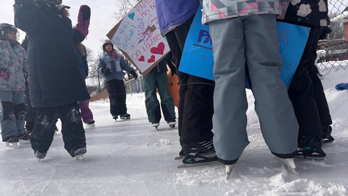 Des enfants patinant avec des pancartes affichant des slogans contre la fermeture de la patinoire.
