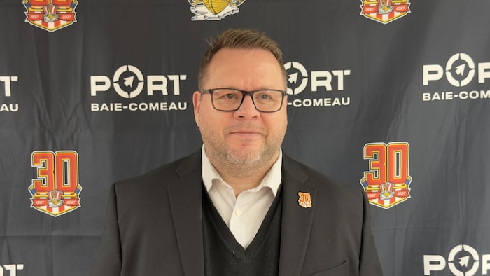 Portrait de Patrice Bosch qui pose devant une toile de fond noire sur laquelle est imprimé le logo du 30e anniversaire du Drakkar de Baie-Comeau.
