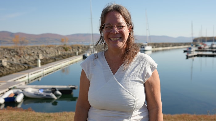 Une femme, Patricia Chartier, se tient souriante devant la marina de Gaspé, il fait beau dehors.