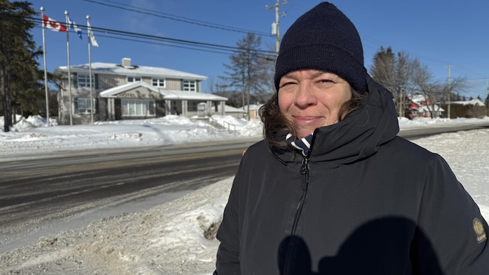 La mairesse de Maria porte un long manteau et une tuque dehors, par une journée ensoleillée.