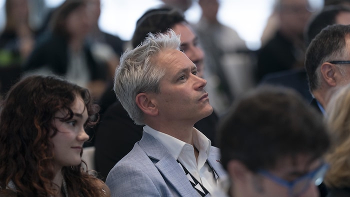 Patrick Bonin écoute dans une salle remplie de participants.