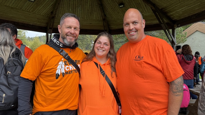 Trois personnes portant des chandails oranges se tiennent côte à côte.