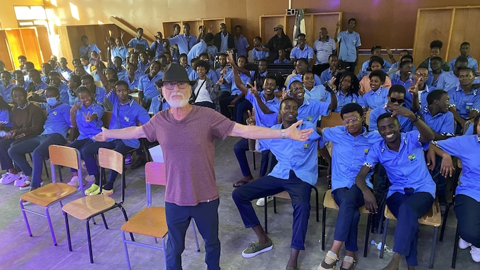 Le chanteur lève ses mains en signe de célébration, entouré d'élèves dans une école.