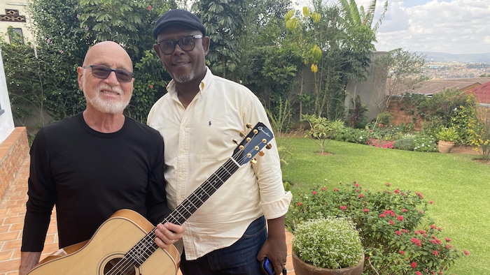 L'artiste pose à côté d'un autre homme, sa guitare dans les mains, à l'extérieur au Rwanda. 