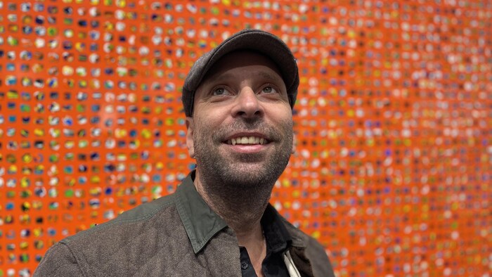 L'artiste Patrick Pépin devant un de ses tableaux. La couleur orange est dominante dans le tableau.