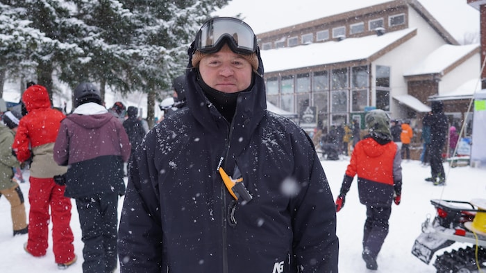 Patrick Trottier, fondateur et co-organisateur du Snowmission, est en tenue de ski avec une tuque et des lunettes, devant un chalet, dans la neige.