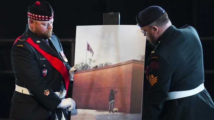 Deux militaires montre un panneau illustrant un partie du projet de monument.