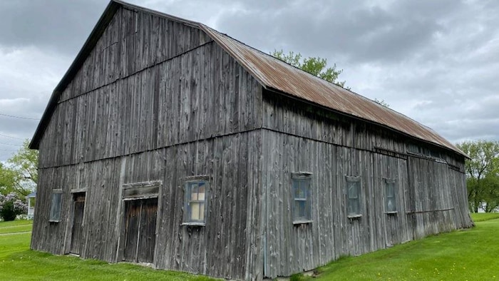 Une grange-étable de taille moyenne en bois gris laisse entrevoir l'âge vénérable du bâtiment.