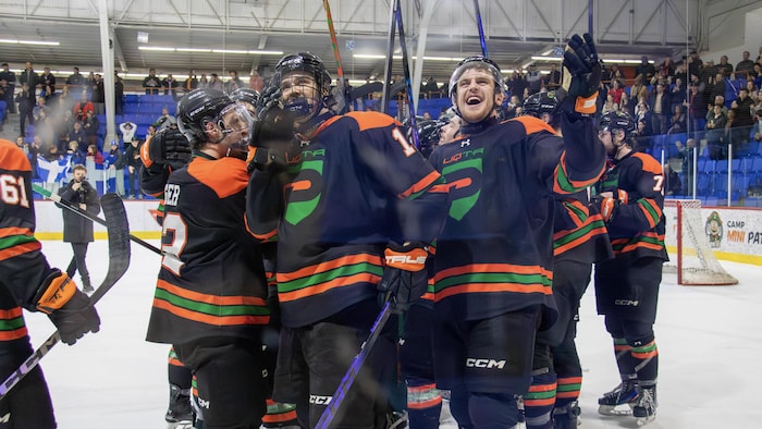 Des joueurs de hockey sur une patinoire saluent la foule.