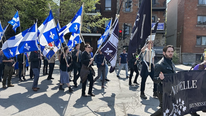 Des jeunes habillés en noir défilent, drapeaux du Québec à la main.