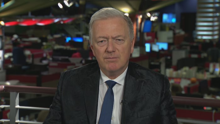 Paul Brunet, dans une salle de nouvelles, regarde la caméra d'un aerial  sérieux. 