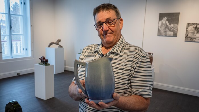 Un homme tient un pichet dans ses mains dans une salle d'exposition de musée.