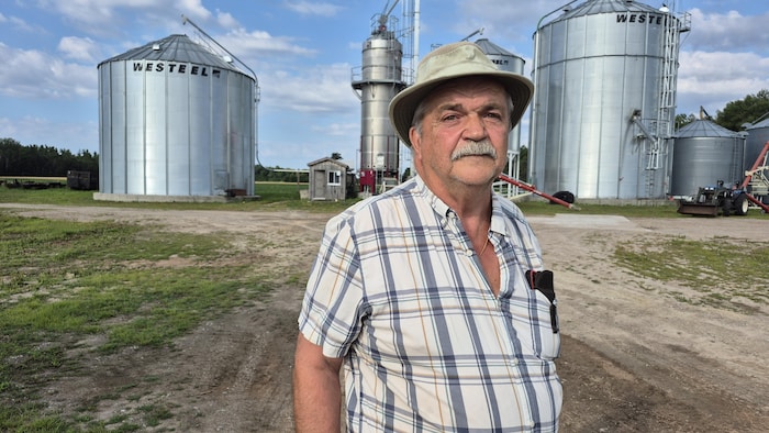 L'agriculteur pose sur son terrain, devant des silos.