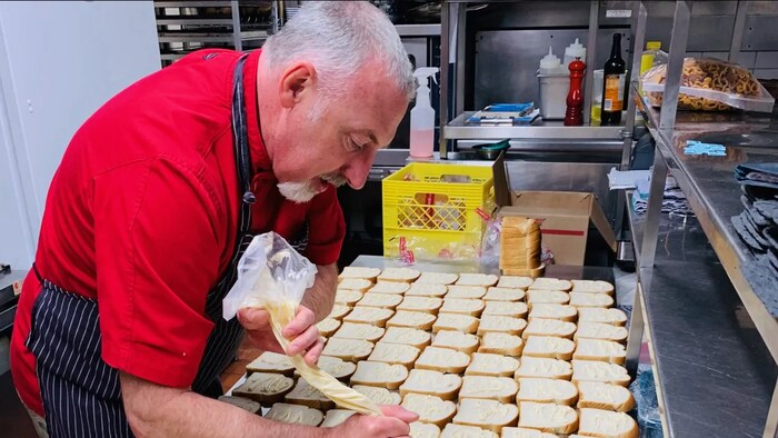 Paul Rogalski met de la mayonnaise sur une rangée de tranches de pain.