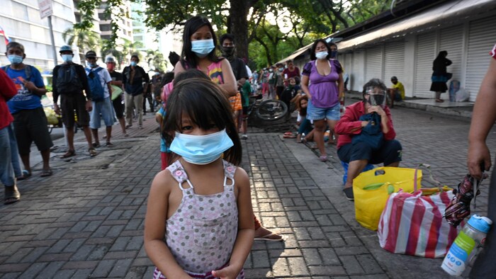 Ang mga tao, kasama ang isang batang babae, ay pumila sa bangketa.