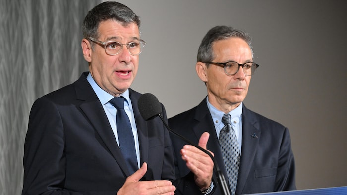 Éric Duhaime gesticule devant un micro aux côtés d'Adrien Pouliot, debout derrière un pupitre.