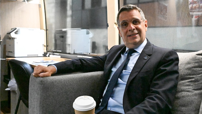 Éric Duhaime sourit, assis dans un sofa à bord de son autobus de campagne, un gobelet de café à la main.