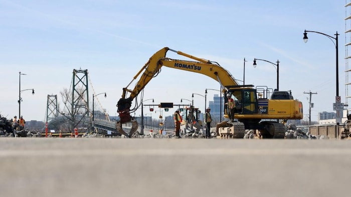 Une grue Komatsu jaune et des travailleurs à une extrémité d'un pont.