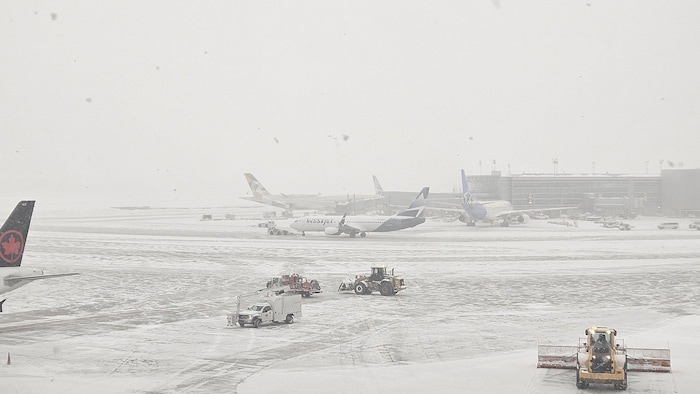 Des équipes de l'aéroport sur le tarmac en train de déblayer la neige.
