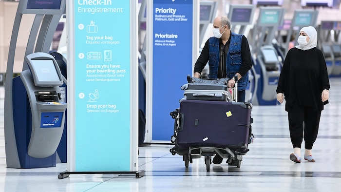 Deux voyageurs près d'un kiosque d'enregistrement de bagages à l'aéroport Pearson.