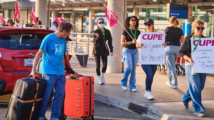 Des voyageurs passent devant des agents de bord d'Air Canada en grève à l'aéroport international Pearson de Toronto, le samedi 16 août 2025.