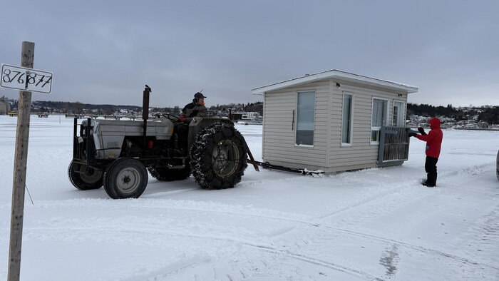 Un tracteur tire une cabane sur une baie gelée.