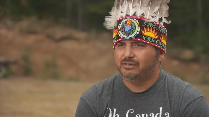 Un homme portant un couvre-chef autochtone pose devant la caméra.