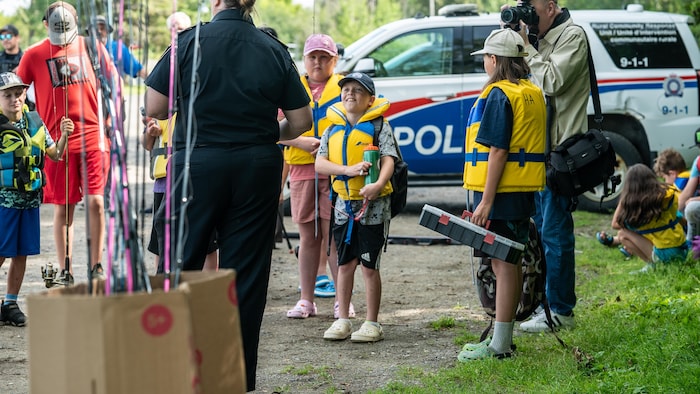 Un enfant écoute attentivement les instructions d'une policière. Il est entouré d'autres enfants et de cannes à pêche.