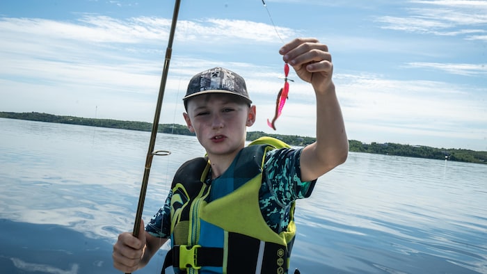 Un enfant montre l'hameçon accroché au bout de sa canne à pêche à bord d'un bateau lors de l'activité.