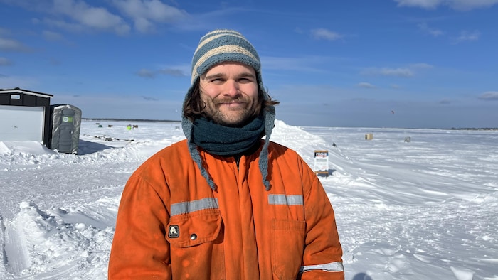 Un homme debout sur une étendue de neige sourit pour la photo sous un ciel bleu.